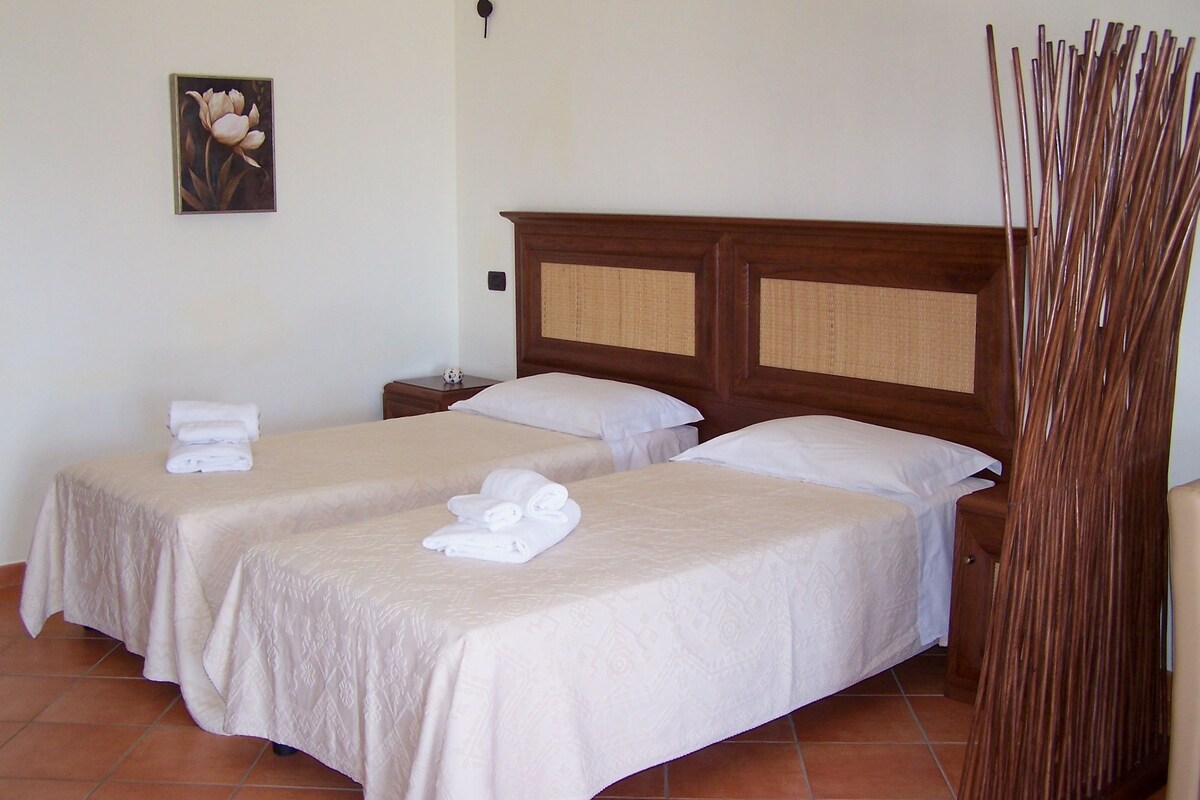 A hotel room with two beds, a wooden headboard, a wall-mounted lamp, and a decorative wall piece.