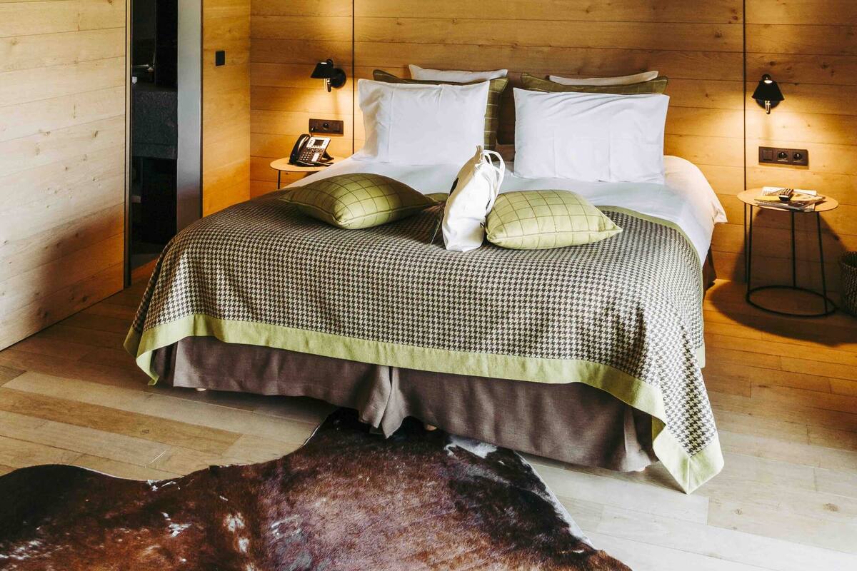 A bedroom with a wooden ceiling, a bed with a checkered bedspread, two bedside lamps, and a wooden floor.