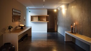 Um interior moderno com uma mesa de recepção, um espelho fixado na parede e um banco com velas.
