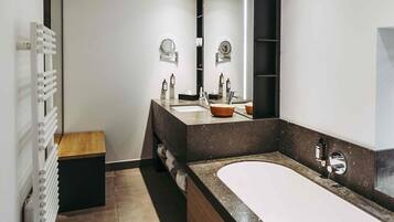 A modern bathroom with a large bathtub, a vanity with a mirror, and a towel rack.