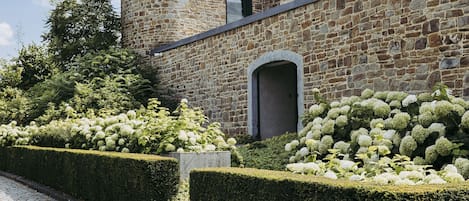A stone building with a rounded tower, a paved pathway, and neatly trimmed hedges.