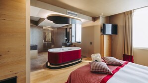 Quarto de hotel moderno com uma cama grande, um edredom xadrez vermelho e branco, uma banheira de veludo vermelha, um espelho grande e uma TV de tela plana montada na parede.