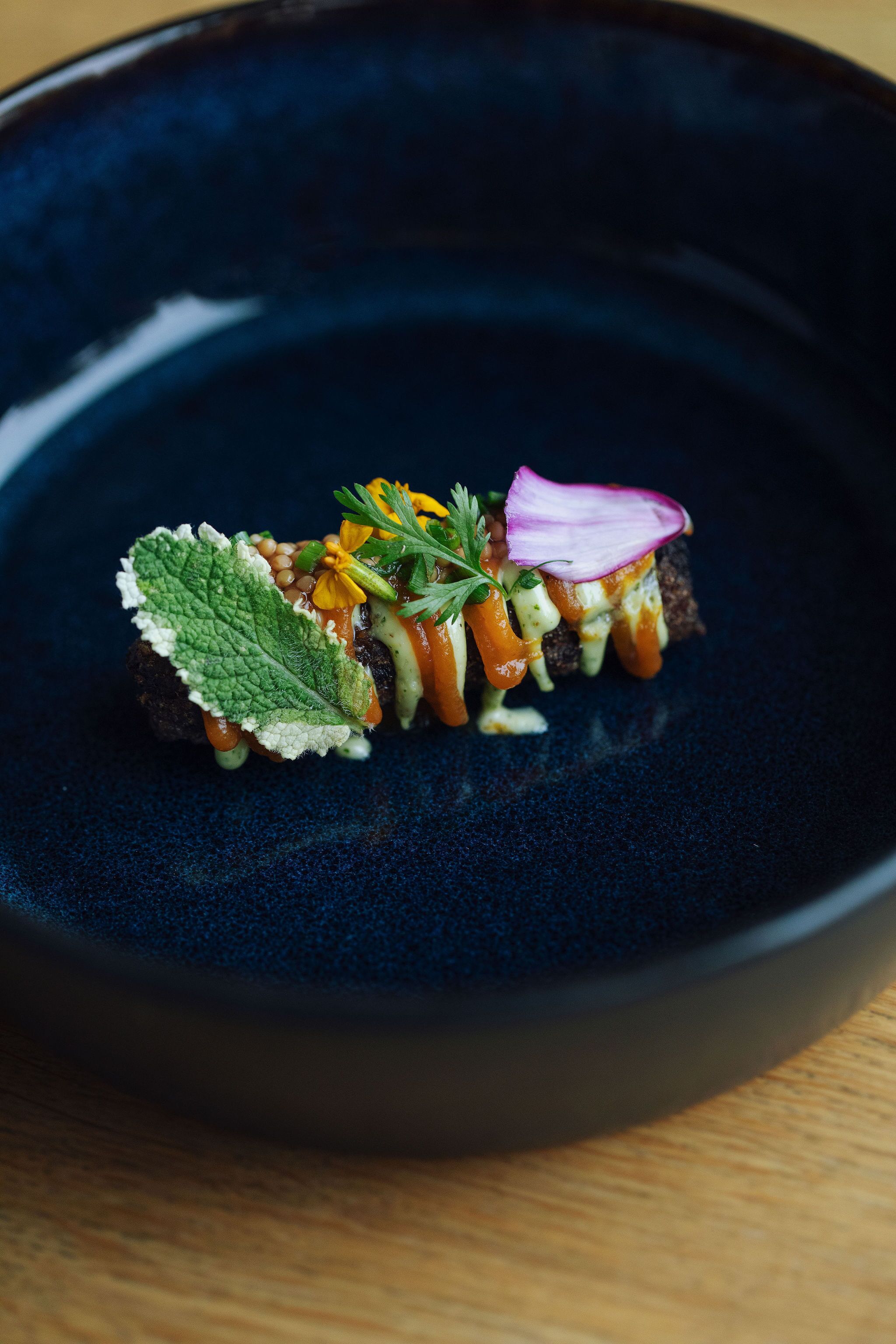 A dark blue plate with a food item that includes a slice of bread, vegetables, and a garnish.