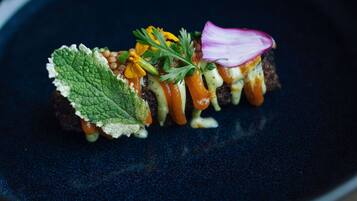 A dark blue plate with a food item that includes a slice of bread, vegetables, and a garnish.