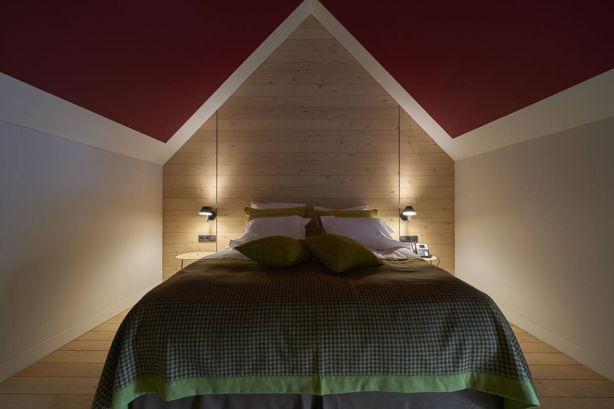 A bedroom with a sloped ceiling, wooden walls, and a bed with a green checkered bedspread.