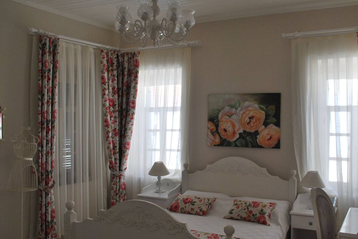 A bedroom with a bed, two nightstands, a chandelier, and floral curtains.