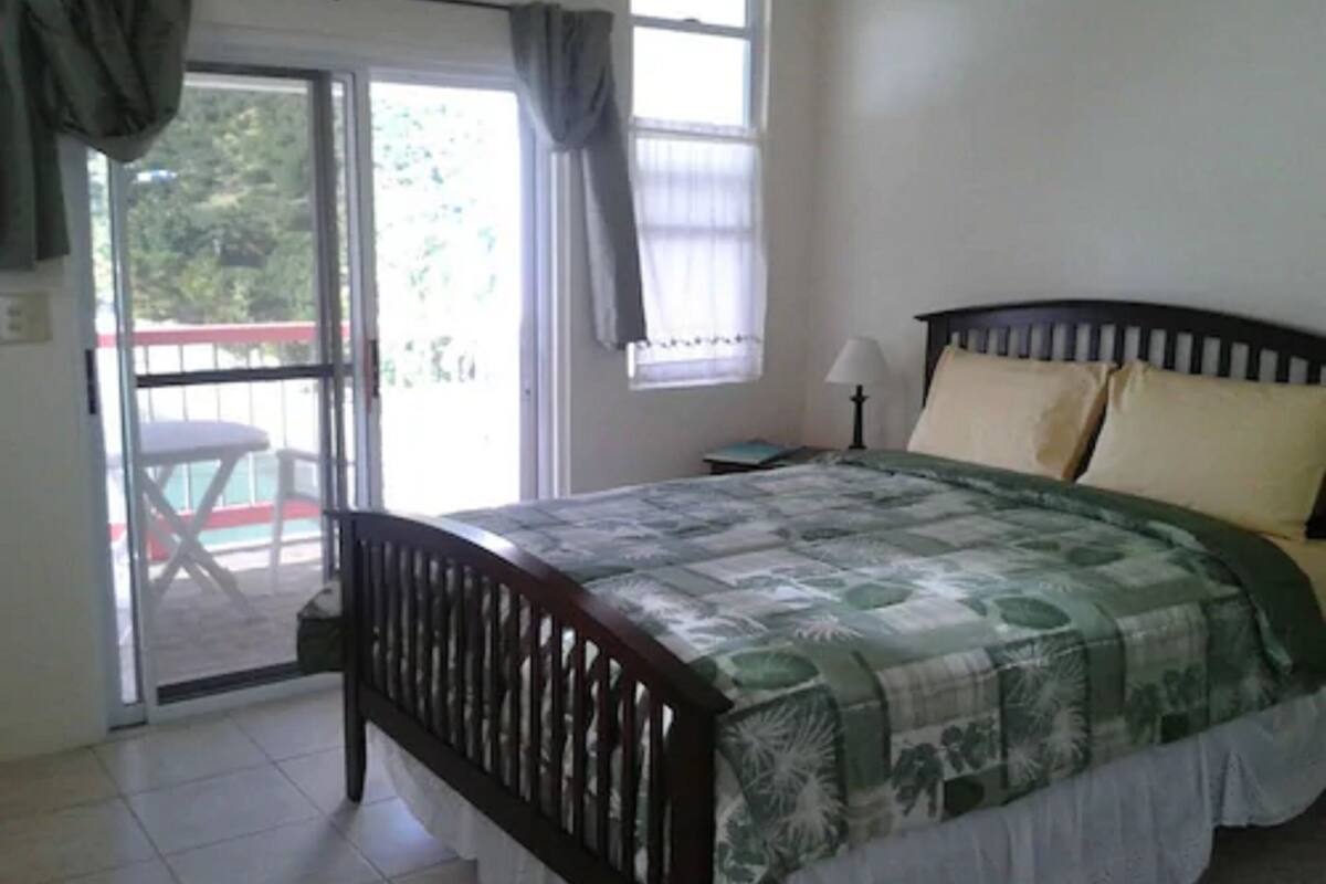 A bedroom with a bed, a nightstand, a lamp, and a view of the outside through a sliding door.
