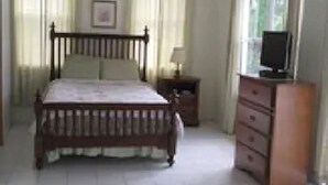 A bedroom with a wooden bed, a nightstand, a dresser, and a window. - Sea Crest Inn (Jost Van Dyke)