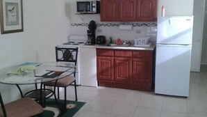 A compact kitchen with a stove, microwave, and refrigerator. There is a dining table with chairs and a small rug. - Sea Crest Inn (Jost Van Dyke)