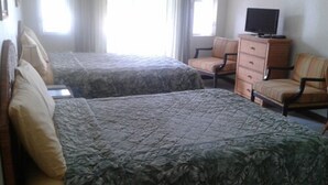 A hotel room with two beds, a television on a dresser, and a window with curtains. - Sea Crest Inn (Jost Van Dyke)