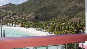 A beach view with a mountain in the background, a clear sky, and a red railing in the foreground. - Sea Crest Inn (Jost Van Dyke)
