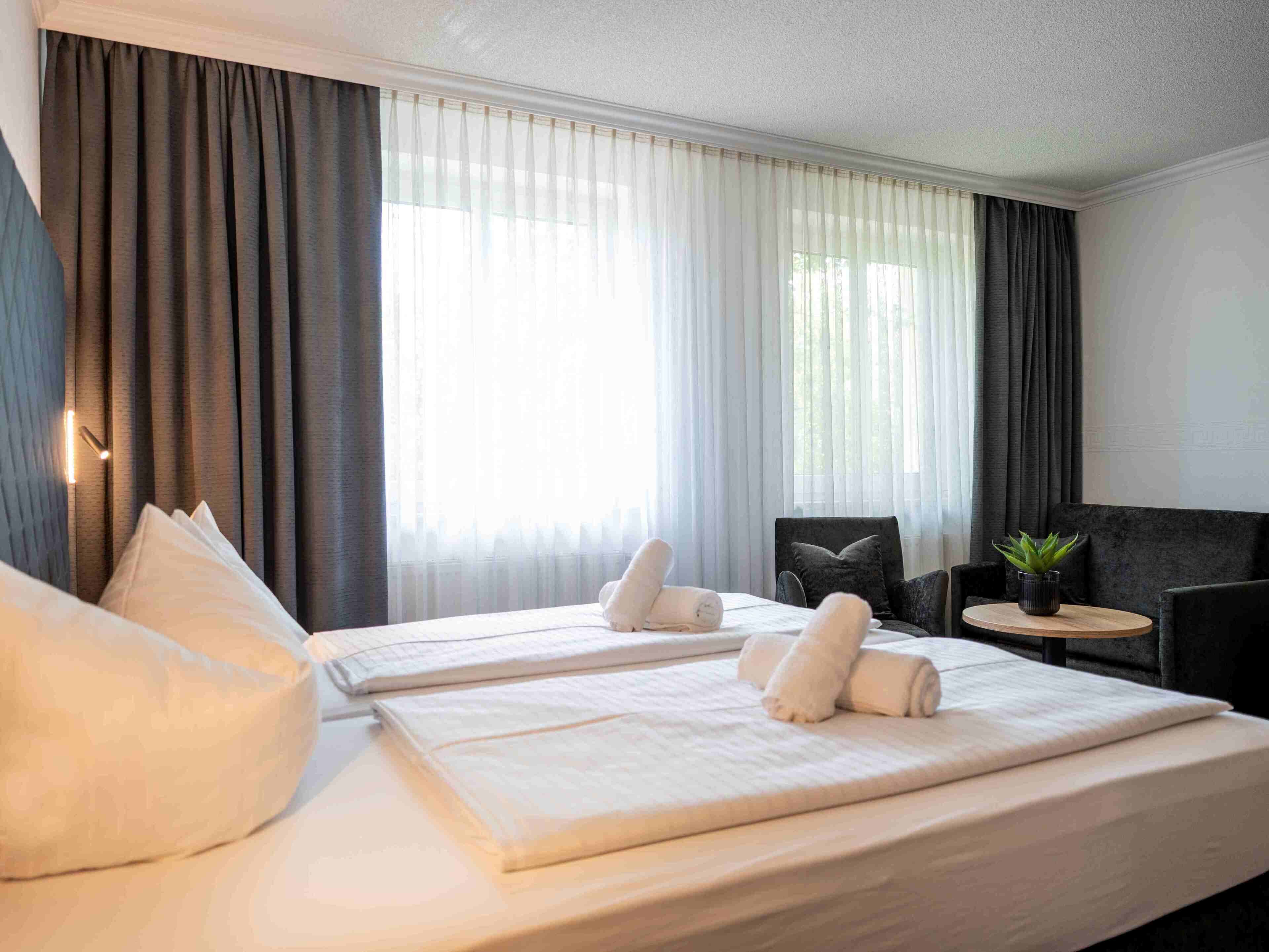 A hotel room with two beds, a small round table, a chair, and a potted plant.