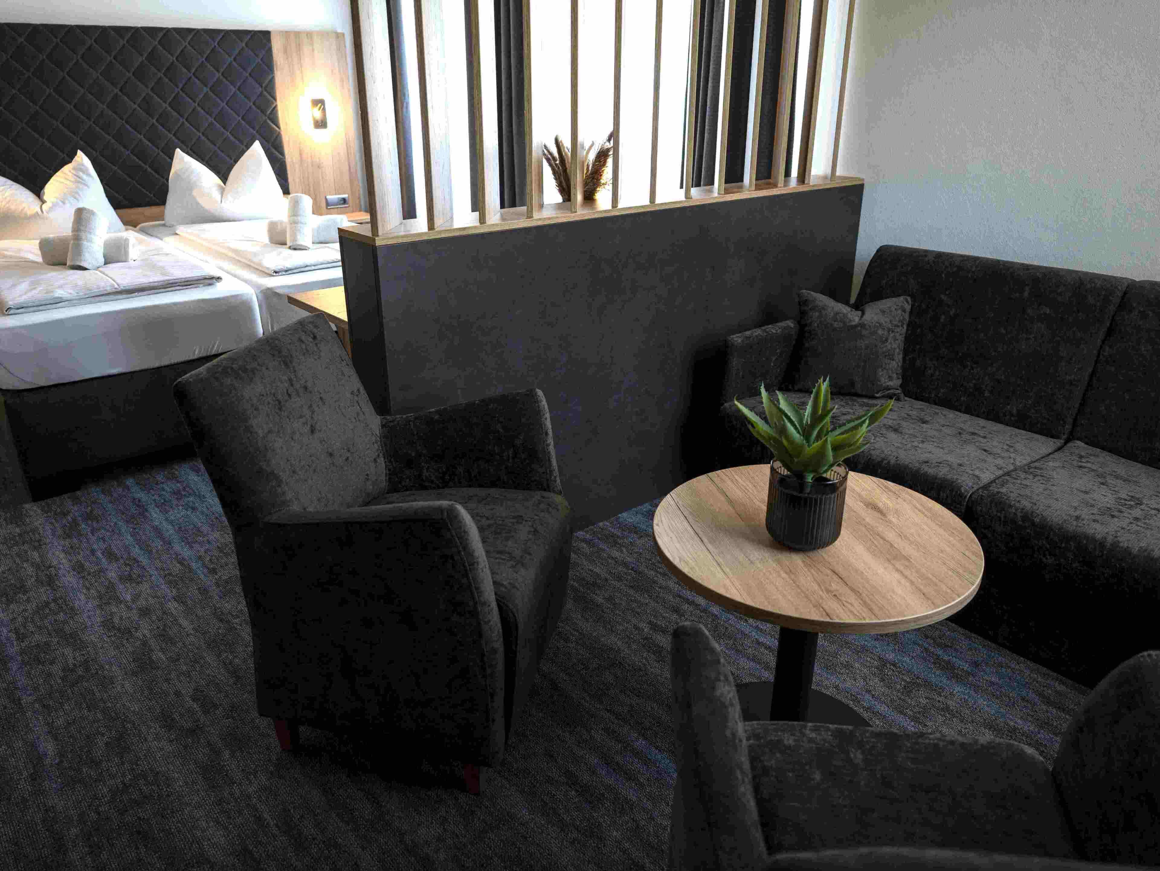 A modern lounge area with dark sofas, a round wooden table, and a potted plant.