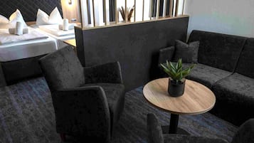 A modern lounge area with dark sofas, a round wooden table, and a potted plant.