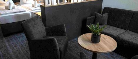Un área de estar moderna con sofás oscuros, una mesa redonda de madera y una planta en maceta.