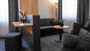 Un salon moderne comprenant un canapé, une table ronde, un petit pouf et une cloison en bois.