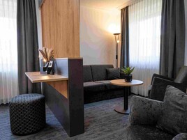 A modern living room with a sofa, a round table, a small ottoman, and a wooden partition.
