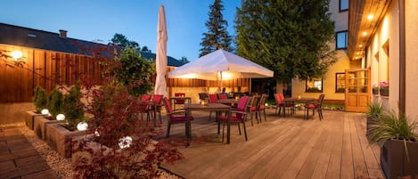 An outdoor patio with wooden flooring, outdoor seating, and a large umbrella.