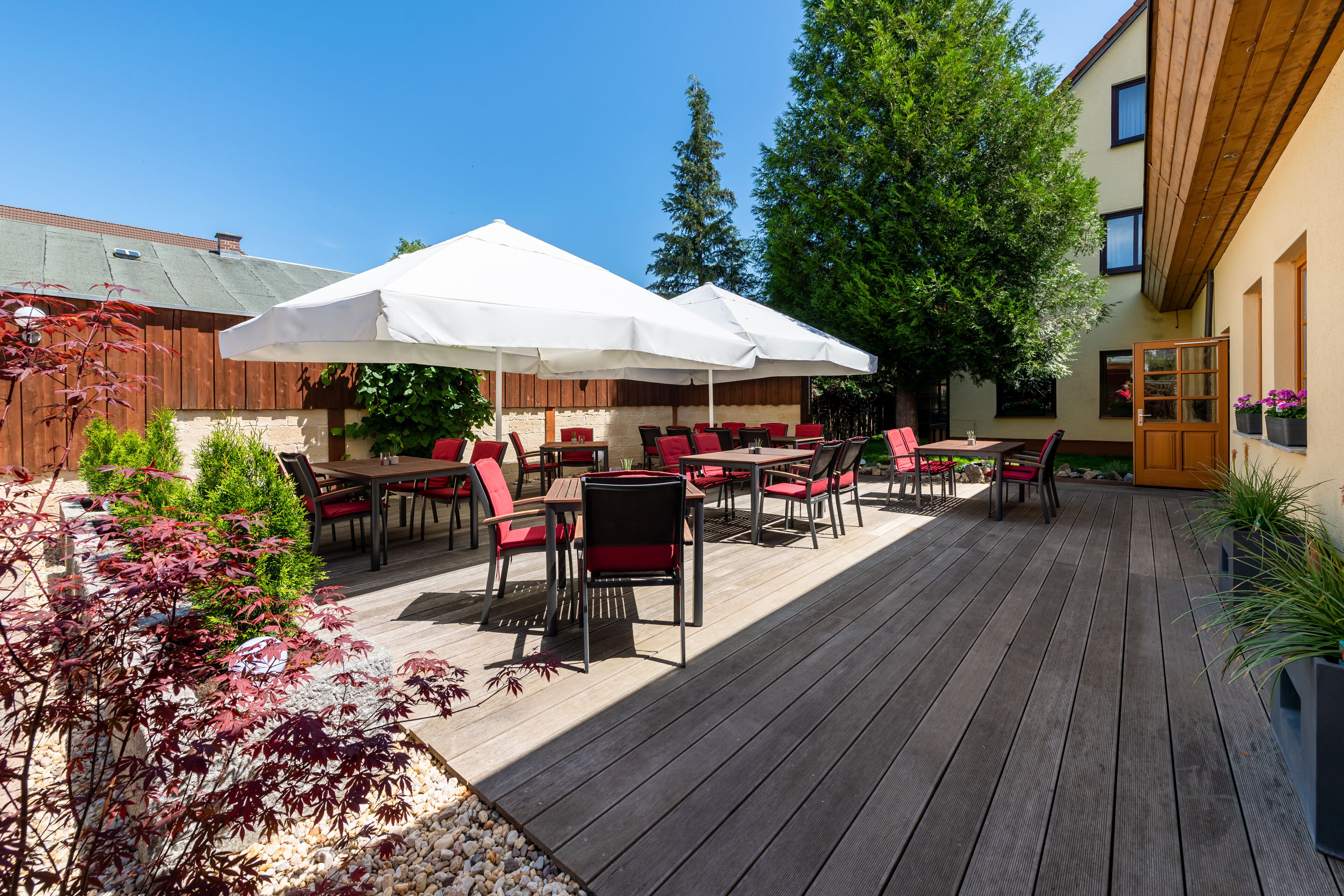 An outdoor patio with wooden flooring, red and black chairs, and white umbrellas.