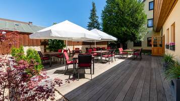 An outdoor patio with wooden flooring, red and black chairs, and white umbrellas.