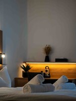 Quarto de hotel com cama bem arrumada, mesa de cabeceira com abajur e uma pequena planta em vaso.