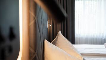 A hotel room with a bed, pillows, a headboard, and a window with curtains.