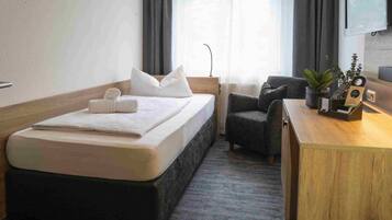 Una habitación de hotel con cama, sillón, escritorio, planta y televisor.