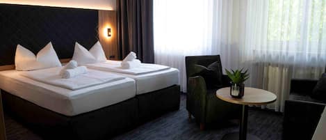 Quarto de hotel com duas camas, uma mesa redonda, uma cadeira e um vaso de planta.