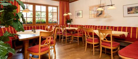 Un restaurant avec des meubles en bois, des banquettes à rayures et une grande fenêtre ornée de plantes.