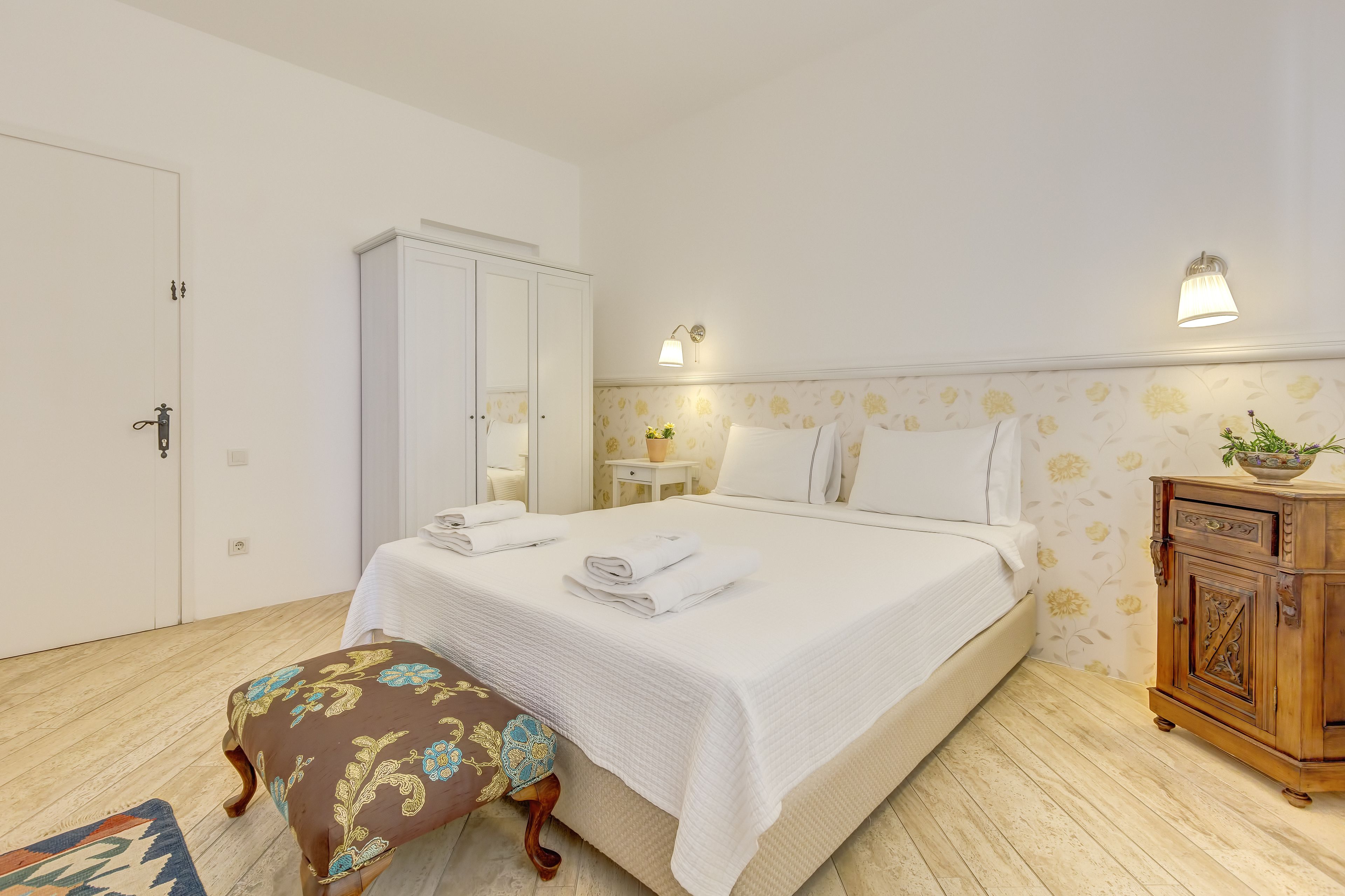 A neatly arranged bedroom with a bed, a wardrobe, a nightstand, and a bench.