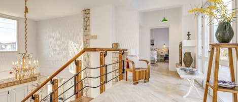 A spacious living area with a wooden staircase, a chandelier, and a view of the kitchen.
