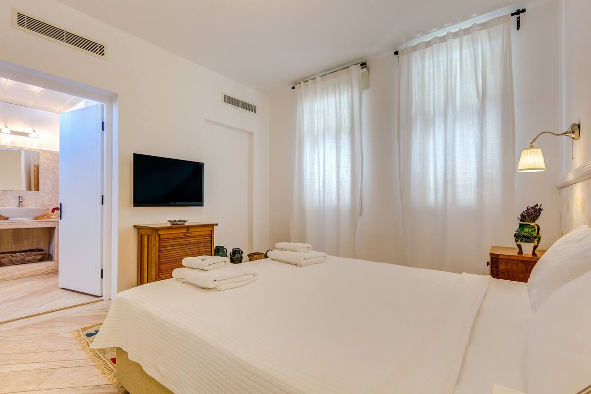 Een hotelkamer met een bed, een televisie, een nachtkastje, een lamp en een badkamer die door een geopende deur zichtbaar is.