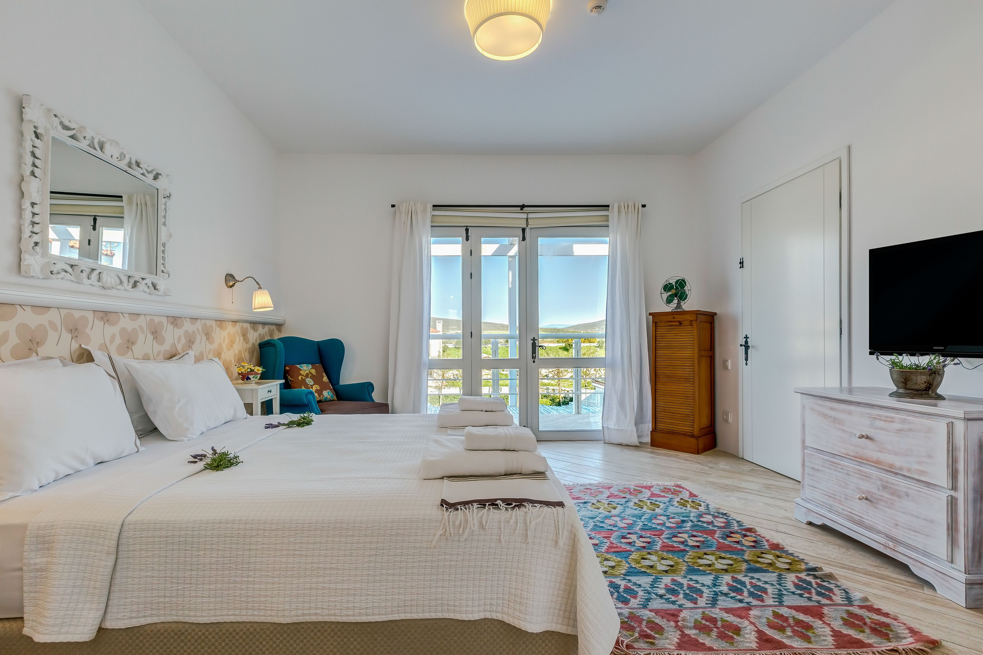 Un dormitorio con cama, cómoda, televisor y vistas al exterior a través de un ventanal.