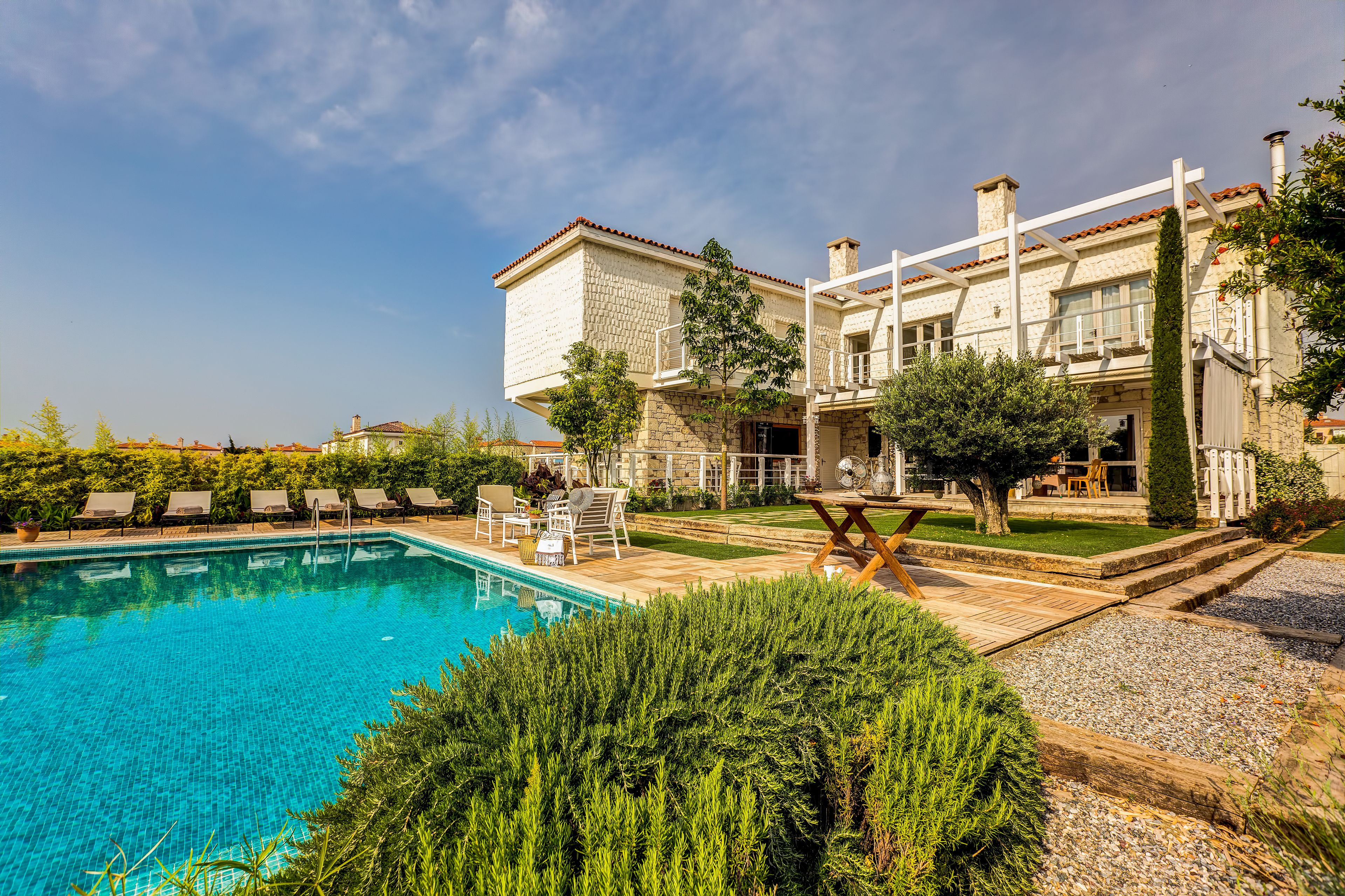 A pool area with a clear blue pool, surrounded by lounge chairs and a wooden deck.