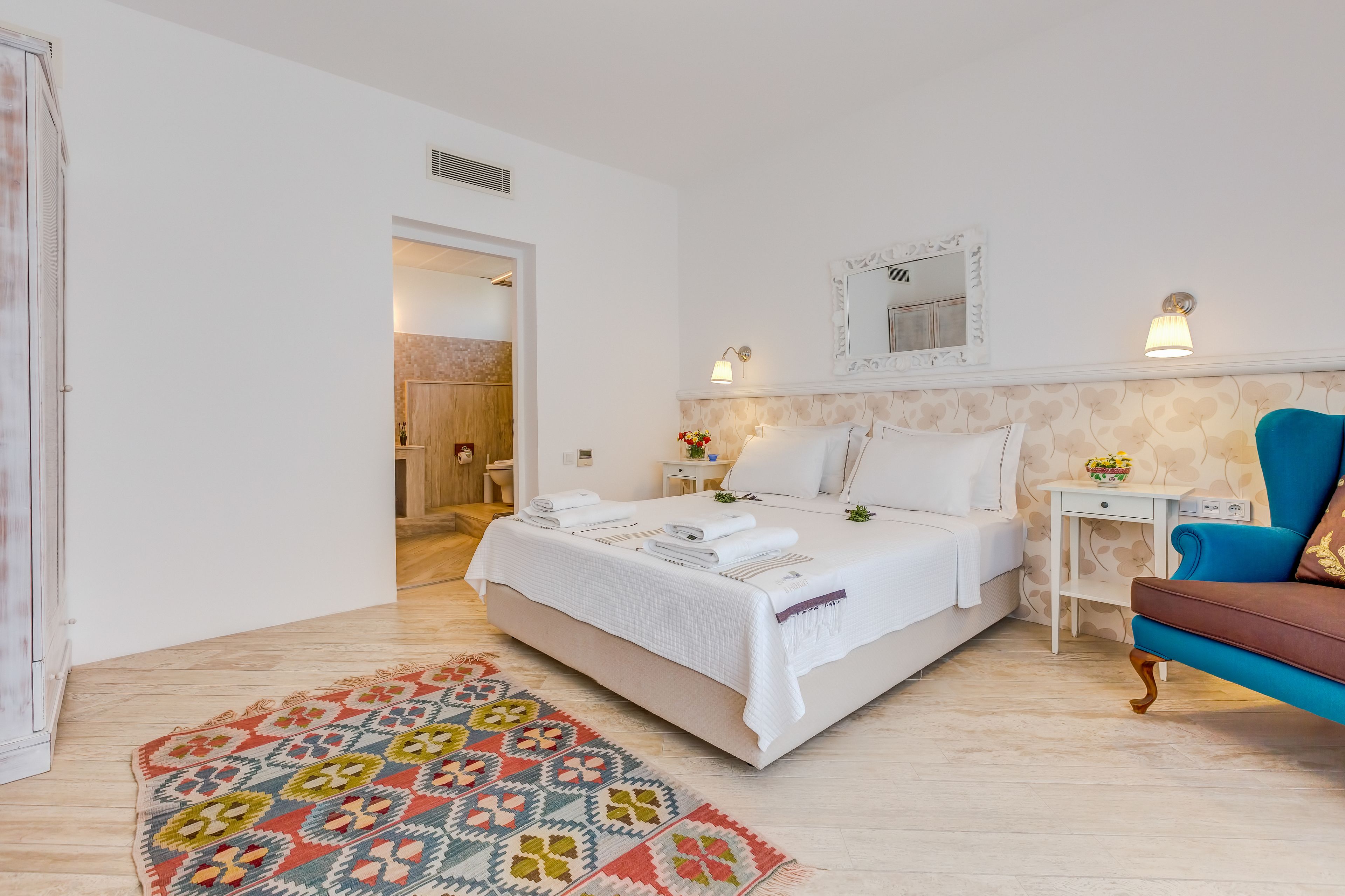 Un dormitorio con una cama, mesitas de noche, un sofá azul y una alfombra estampada.