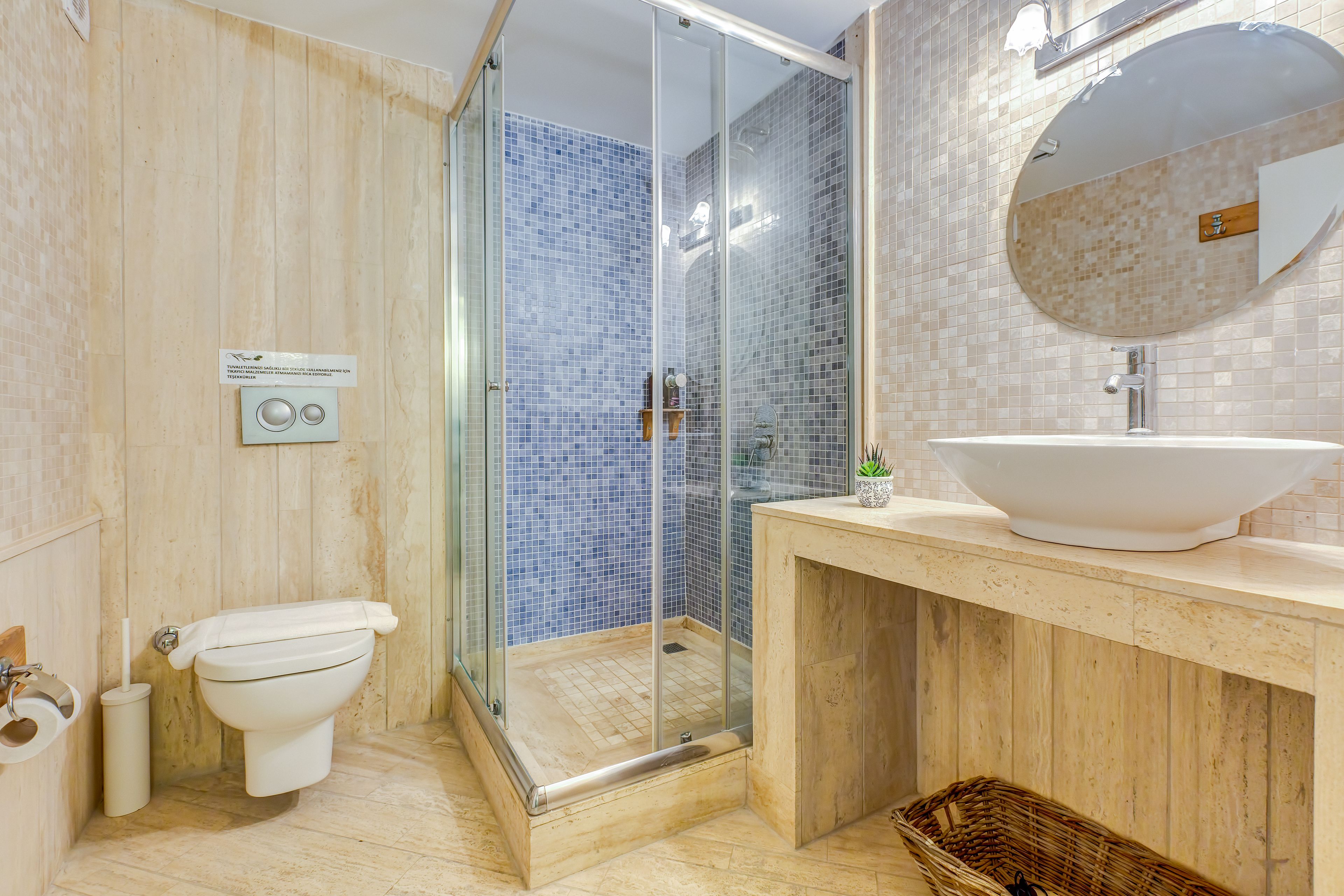 Ein Badezimmer mit einer gläsernen Dusche, einer Toilette, einem Waschbecken mit großem Spiegel und einer gefliesten Rückwand.