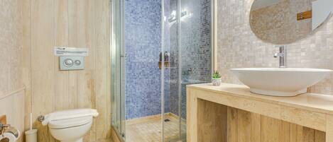 Un baño con ducha de vidrio, inodoro, lavamanos con un espejo grande y salpicadero de azulejos.