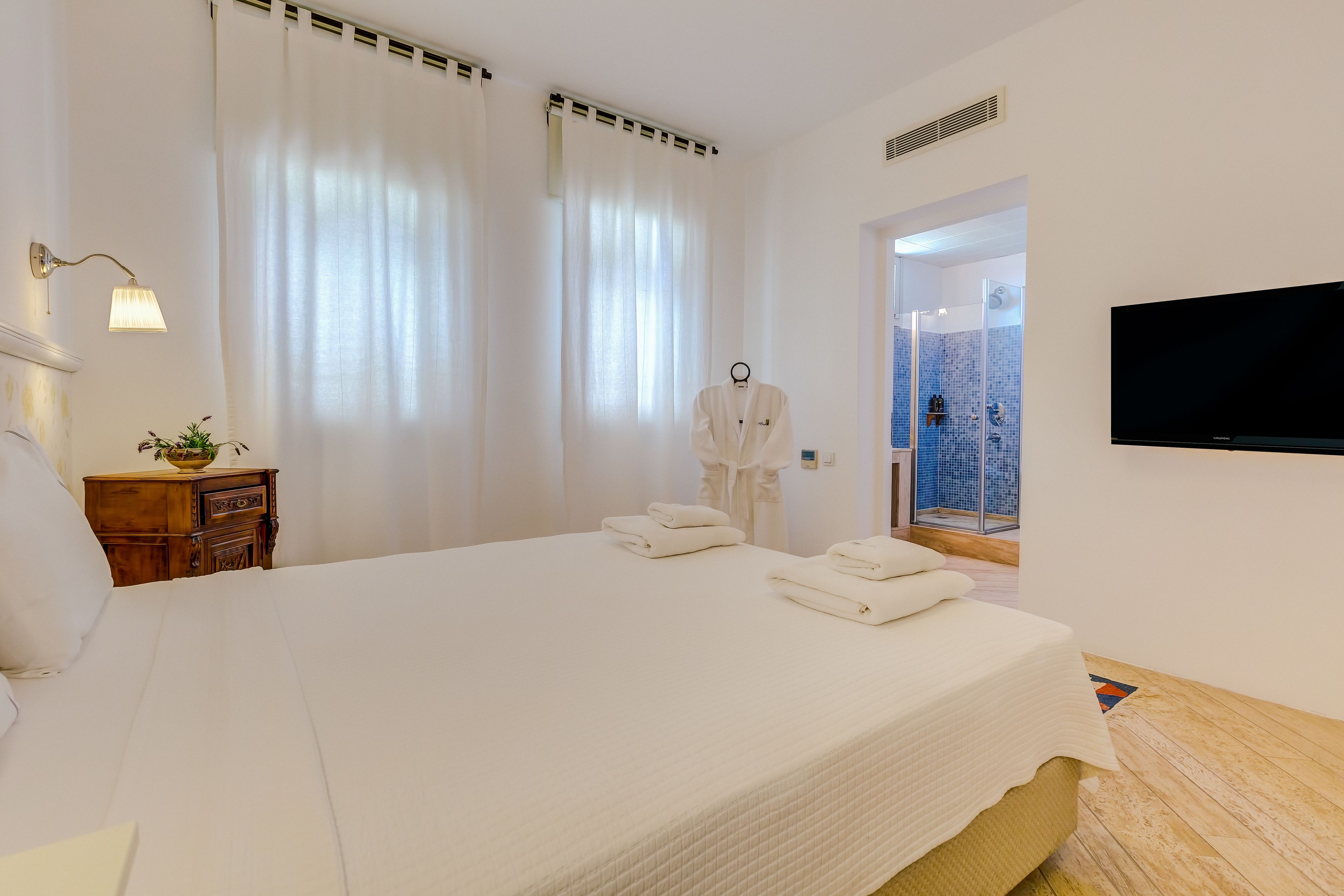 A hotel room with a large bed, a TV, a wooden dresser, and a view of a blue-tiled room.