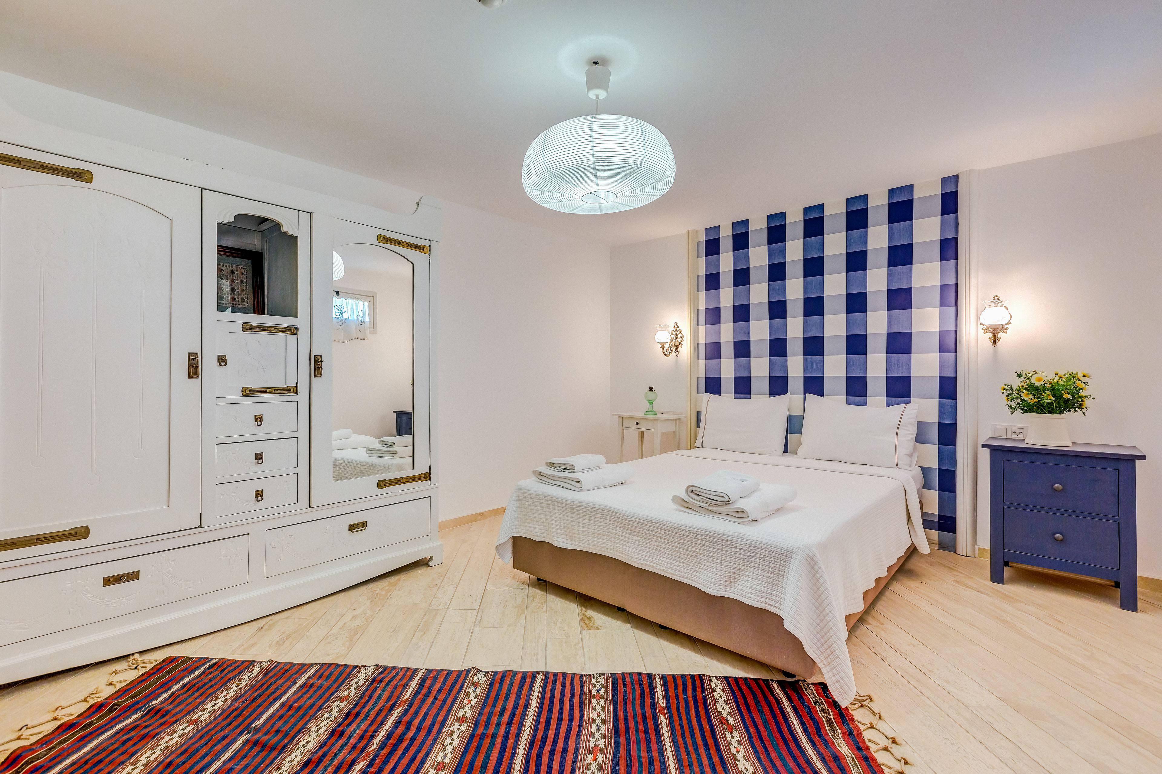 A bedroom with a bed, bedside table, nightstand, wardrobe, and a patterned rug.