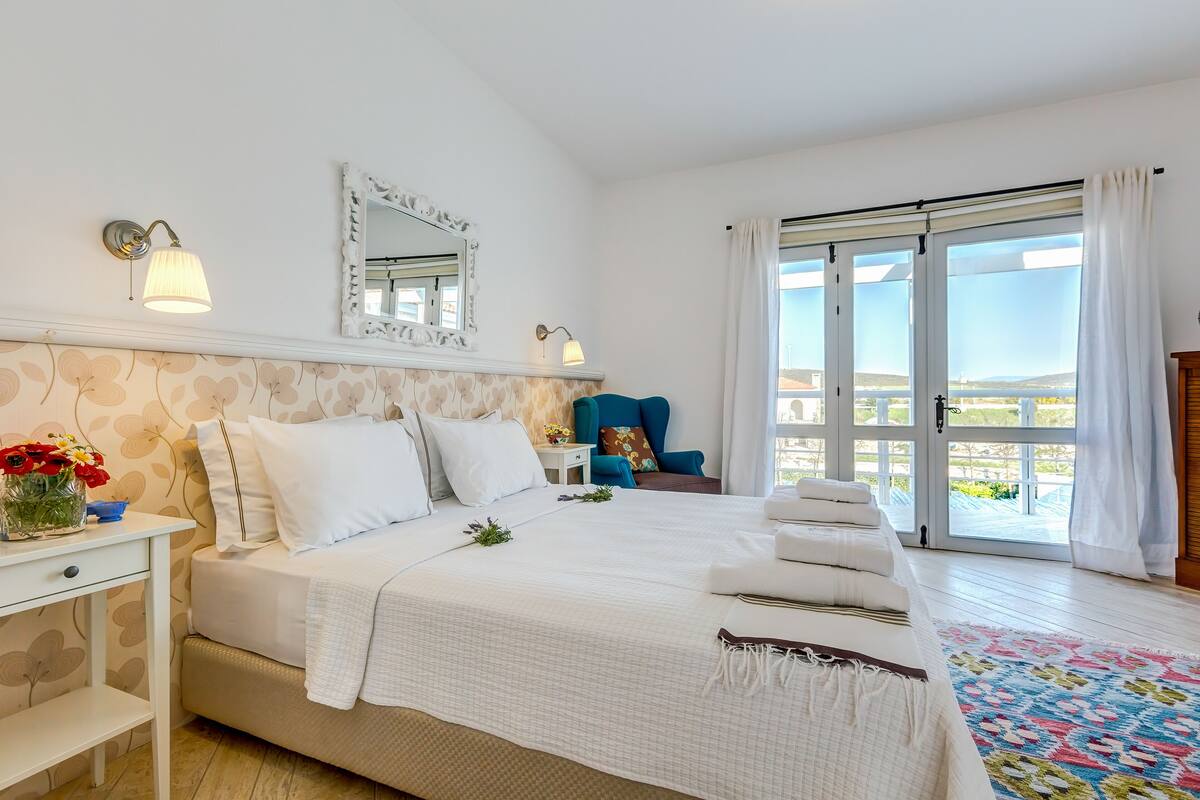 Een slaapkamer met een groot bed, een nachtkastje, een dressoir, een stoel en een balkon met uitzicht.