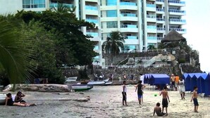 A beach with people, boats, and a large building in the background.