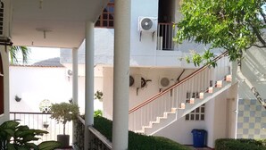 A covered outdoor corridor with tiled flooring, white railings, and potted plants.