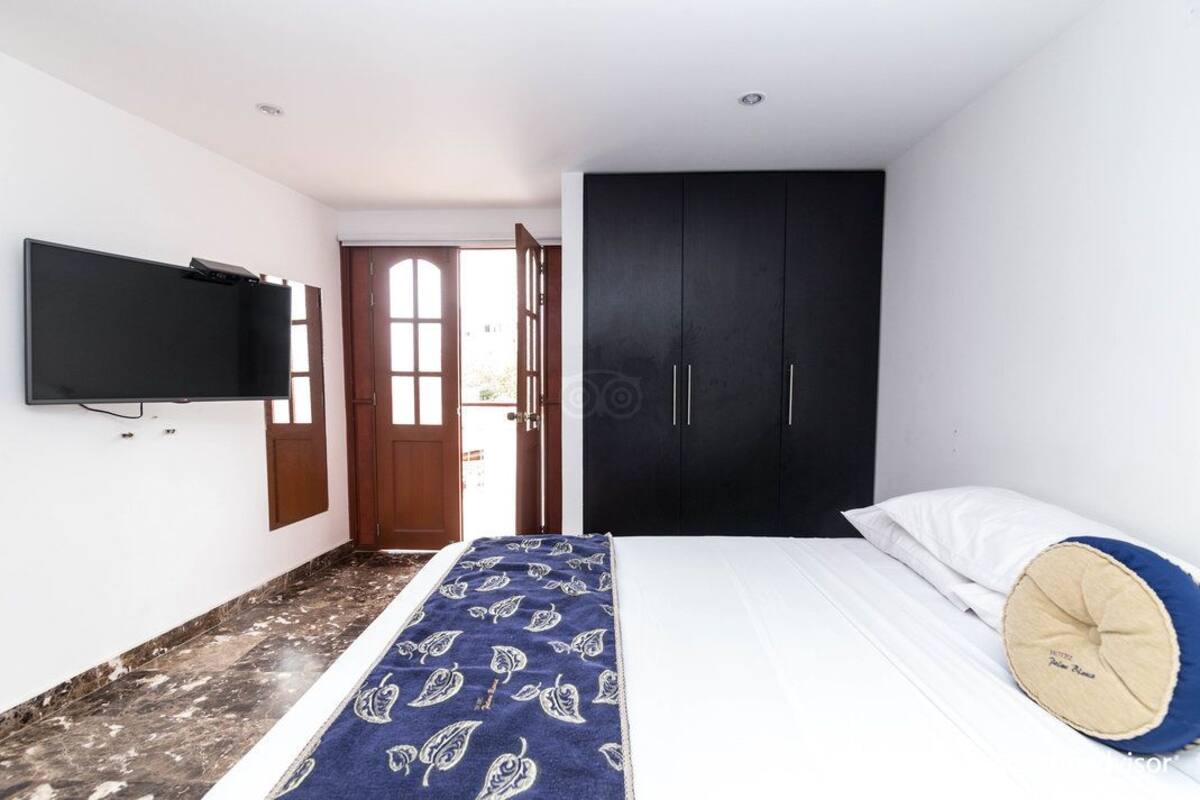 Une chambre à coucher comprenant un lit, un téléviseur fixé au mur, une armoire et une porte donnant sur une autre pièce.