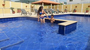 A swimming pool with tiled walls and a sunshade structure in the background.
