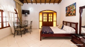 A bedroom with a wooden bed, a desk with a chair, a TV, and a painting on the wall.