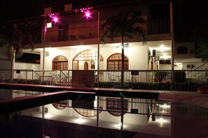 Vista nocturna de un edificio con ventanas arqueadas y una piscina que refleja las luces.