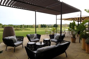 Un espace extérieur aménagé en terrasse, avec des meubles en osier, des tables rondes et des plantes en pot.