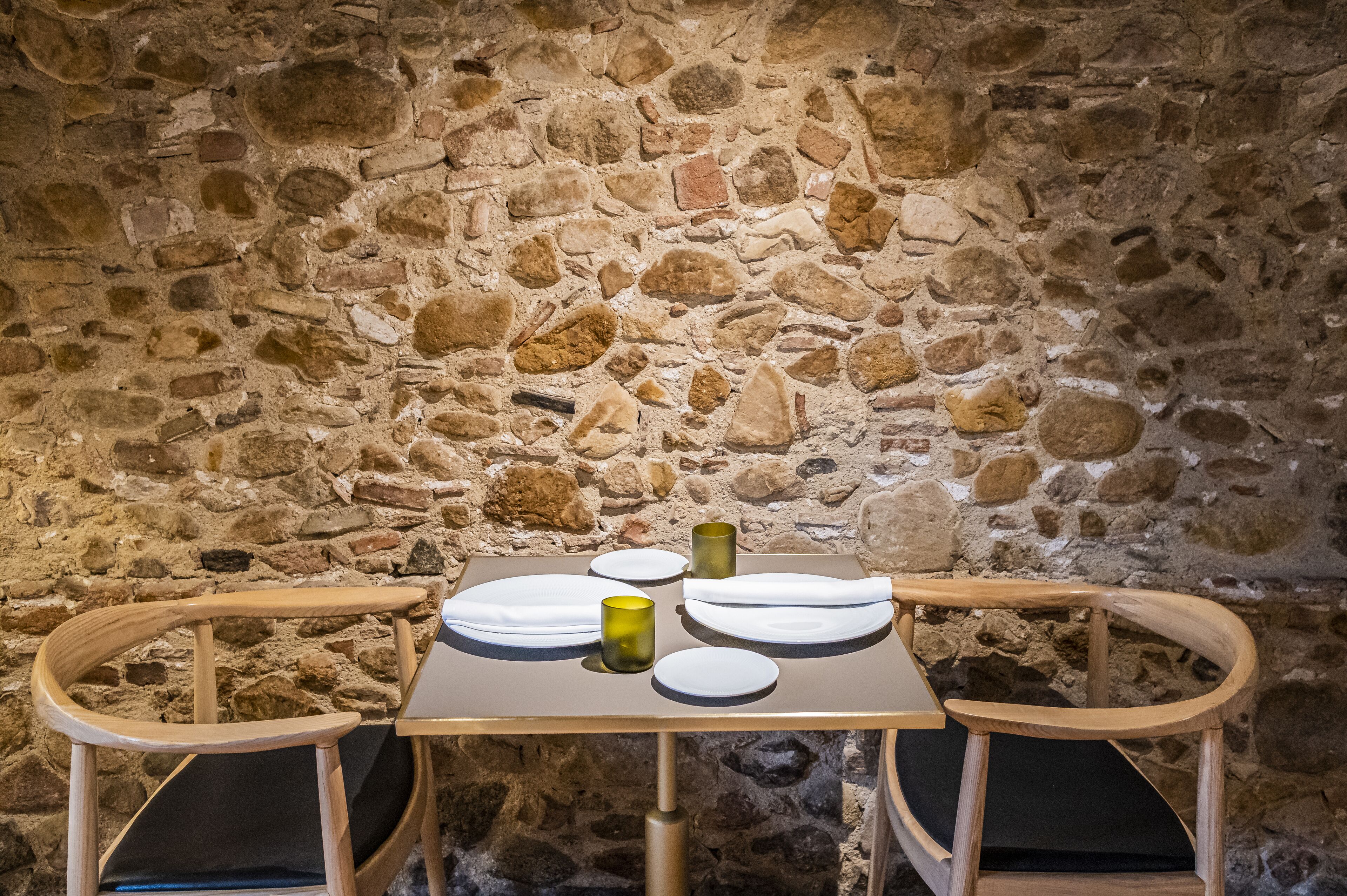 A stone wall with a table set for two, featuring plates, a glass, and a napkin.