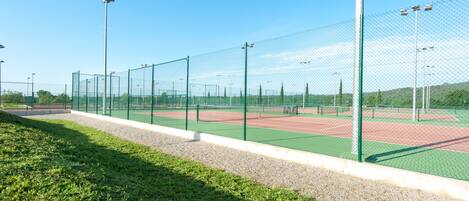 Un campo da tennis con rete, circondato da erba e alberi.