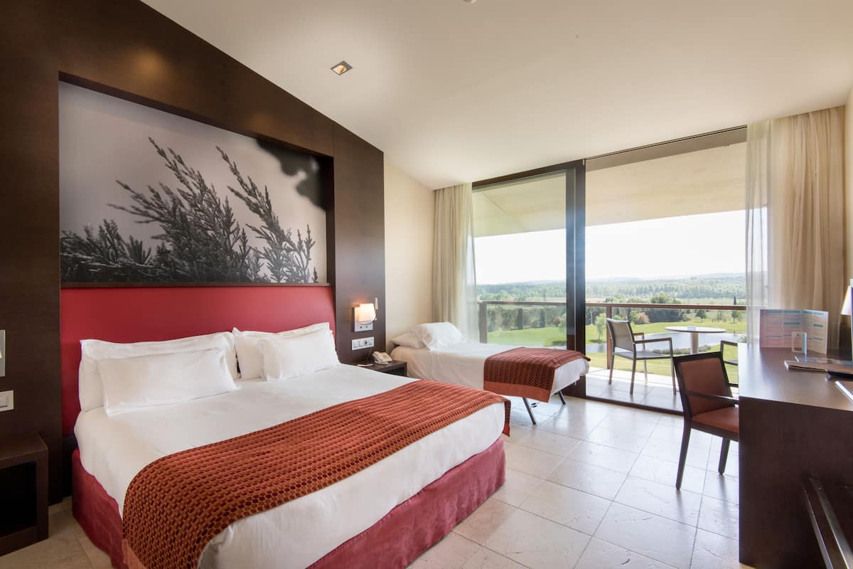 A hotel room with two beds, a desk, and a balcony with a view.